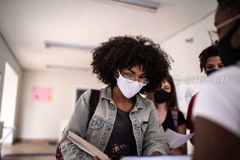 戴口罩的学生在大学/高中走廊向同事展示便签